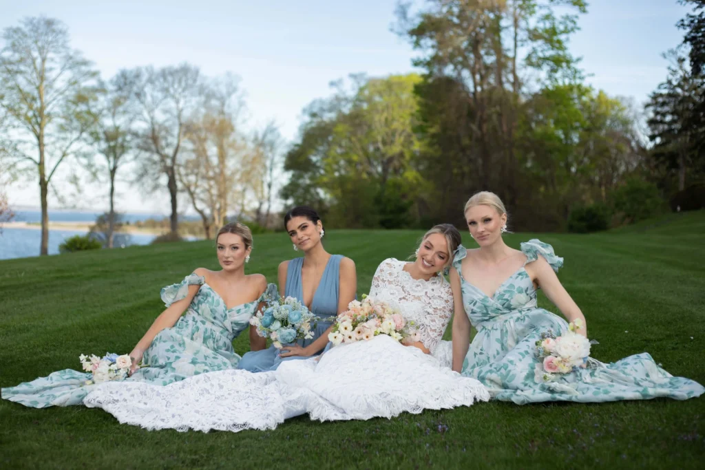 Bride and her girls sitting on the back lawn behind Glen Manor House. Bride is wearing an intricate lace dress and bridesmaids are wearing mismatched blue dresses.