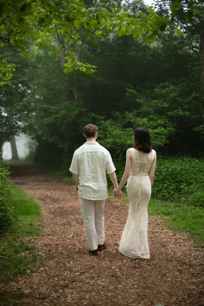 Castle Hill Inn | Kelsey Sheehan Photography Rhode Island Wedding Photographer | A couple holding hands walks on a leafy forest path. The man wears a light shirt and pants, the woman a long dress. The scene feels peaceful and romantic.