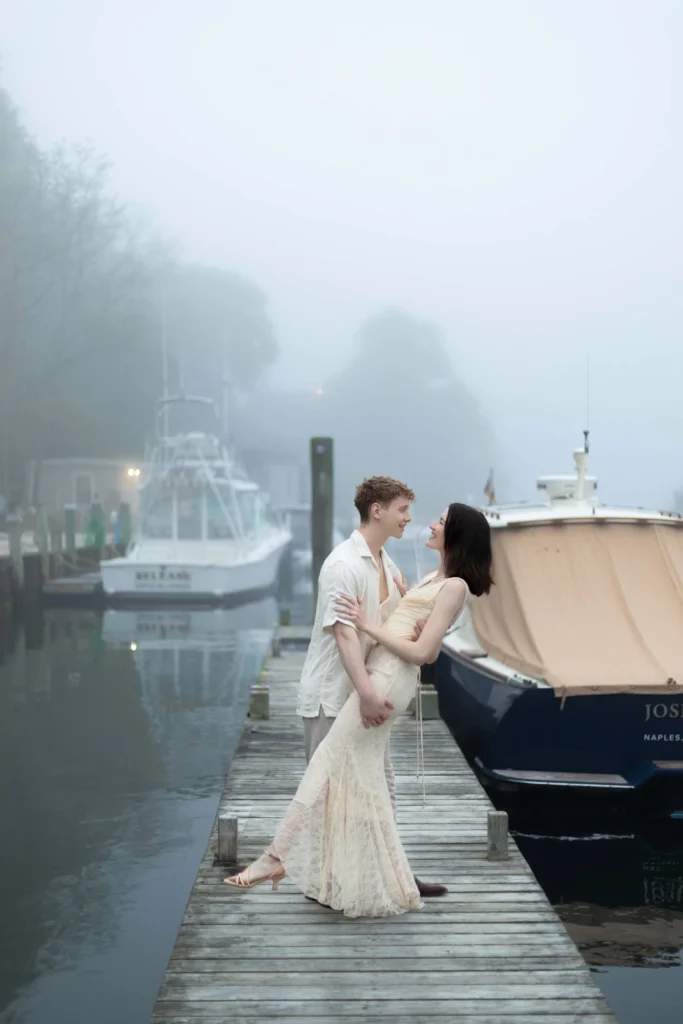 Castle Hill Inn | Kelsey Sheehan Photography Rhode Island Wedding Photographer | A couple stands on a foggy dock, embracing near a yacht. The atmosphere is serene and romantic, set beside calm water with boats hazily visible in the background.