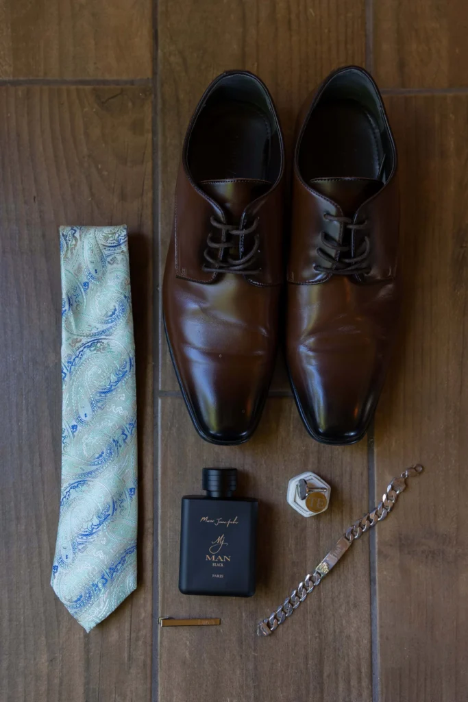 Boston Public Library Engagement Photos Session | Kelsey Sheehan Photography Rhode Island Wedding Photographer | Elegant flat lay of men's accessories on wood: brown shoes, a patterned tie, cologne, a bracelet, tie clip, and a hexagonal ring box. Sophisticated vibe.