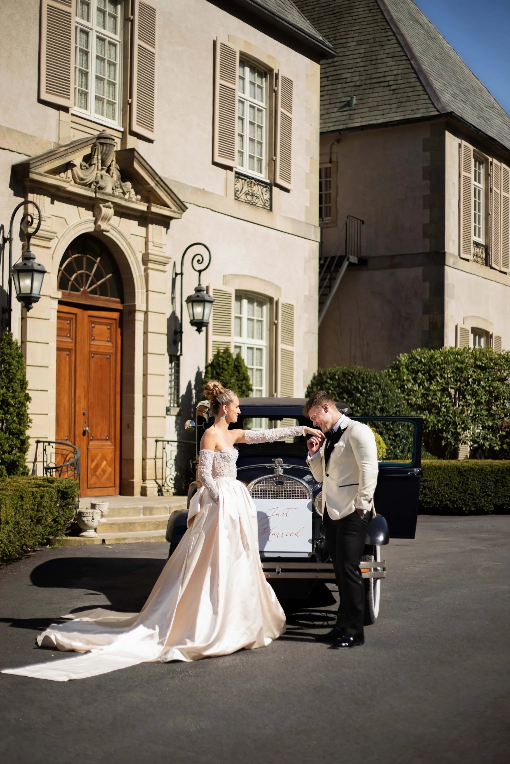 Castle Wedding Venues in New England | Kelsey Sheehan Photography Rhode Island Wedding Photographer | A bride and groom stand by a vintage car, surrounded by elegant architecture. The groom kisses the bride's hand, conveying romance and timeless elegance.