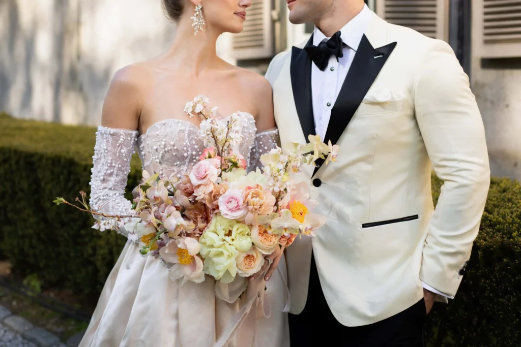 Bride is wearing an sleeveless dress with detached sleeves and a beautiful pink and peach bouquet