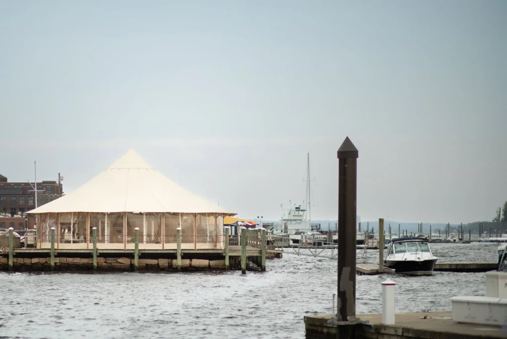 Bristol Harbor Inn | Kelsey Sheehan Photography Rhode Island Wedding Photographer | Calm marina scene with a waterfront gazebo, colorful umbrellas, docked boats, and a soft blue sky. The mood is serene and peaceful.