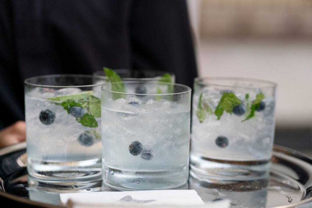 Boston Public Library Wedding | Kelsey Sheehan Photography Rhode Island Wedding Photographer | Four clear glasses filled with a refreshing cocktail featuring ice, blueberries, and mint leaves on a metal tray. The atmosphere is crisp and inviting.