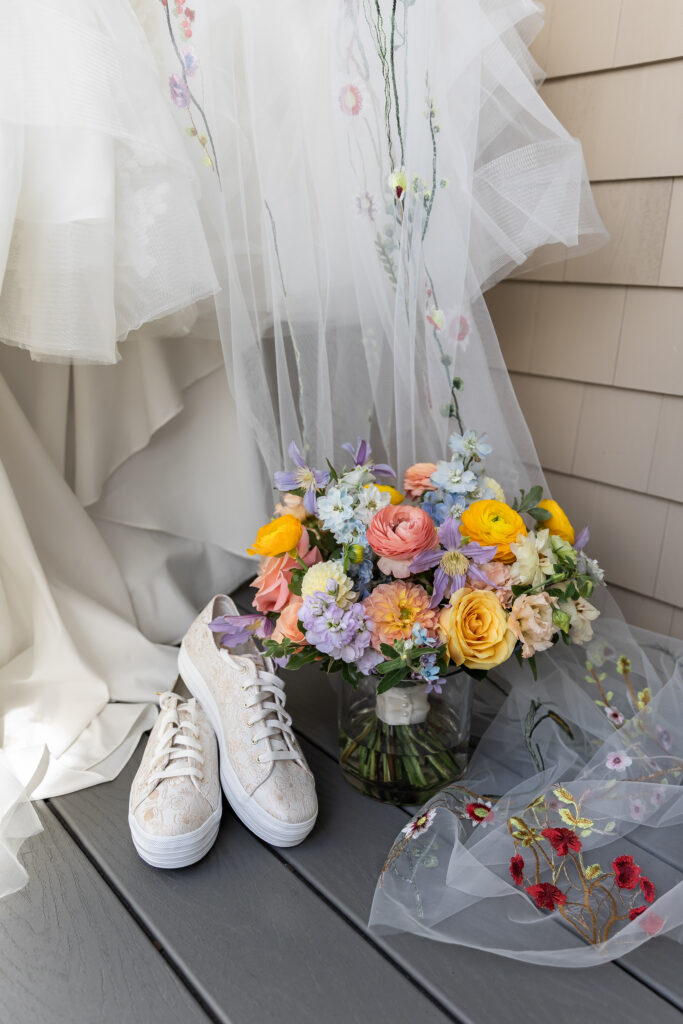 Bristol Harbor Inn | Kelsey Sheehan Photography Rhode Island Wedding Photographer | A bridal scene with lace sneakers, a colorful bouquet of roses and ranunculus, and a veil with floral embroidery on a wooden floor.