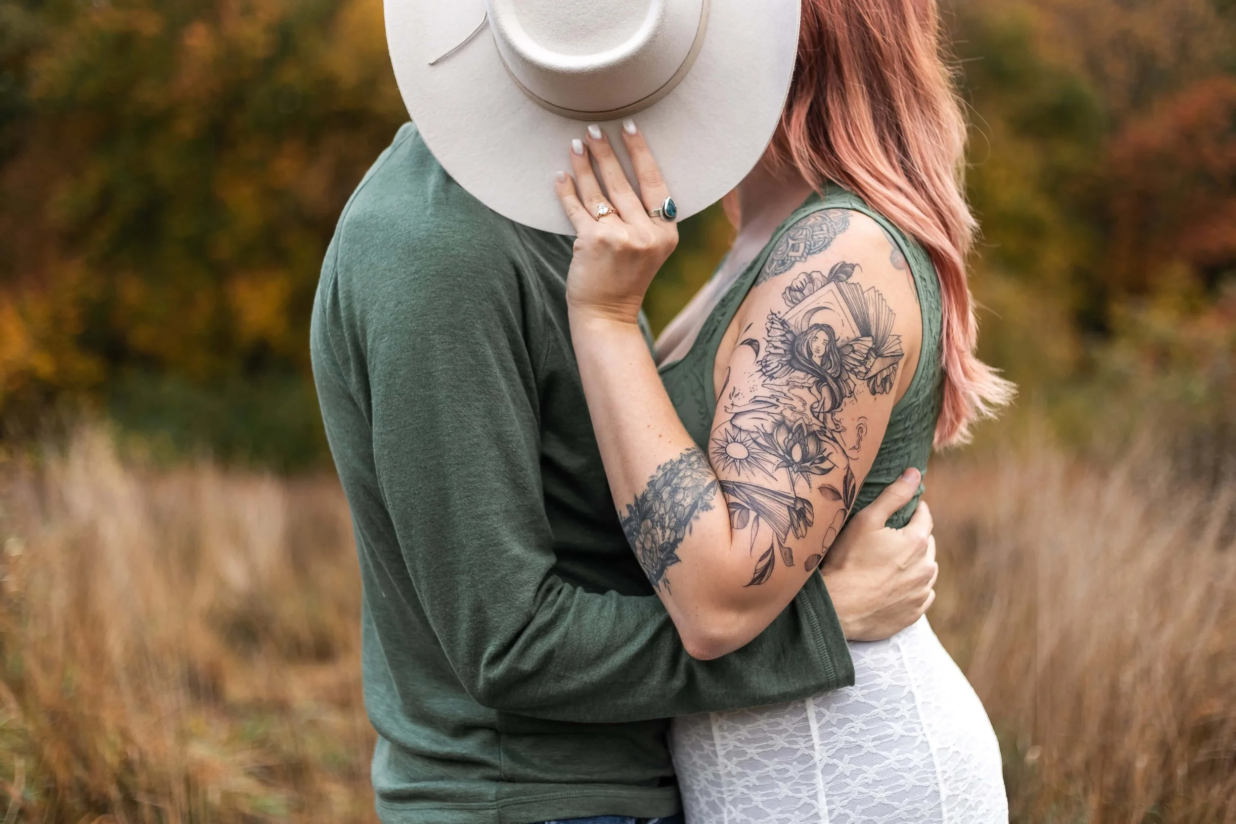Couple kissing behind her cowboy hat in a field just outside Boston, MA. She is wearing a green tank top and lace skirt. He is wearing a long sleeve green shirt. 