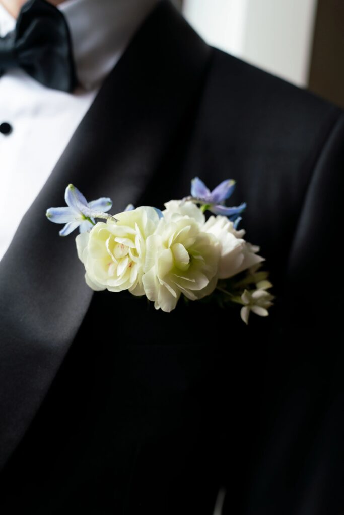 Rosecliff Mansion | Kelsey Sheehan Photography Rhode Island Wedding Photographer | A black tuxedo with a bow tie features a boutonniere of pale green and white flowers, accented with small purple blooms, conveying elegance.