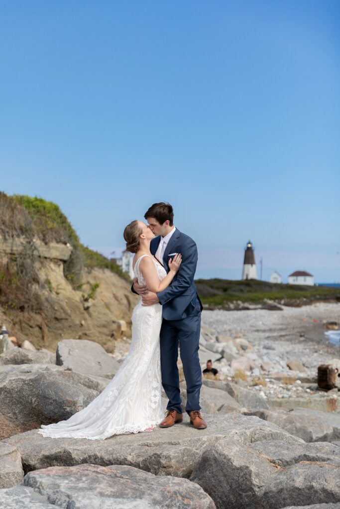 Bride and groom kissing on the rocks with Point Judith Lighthouse in the background